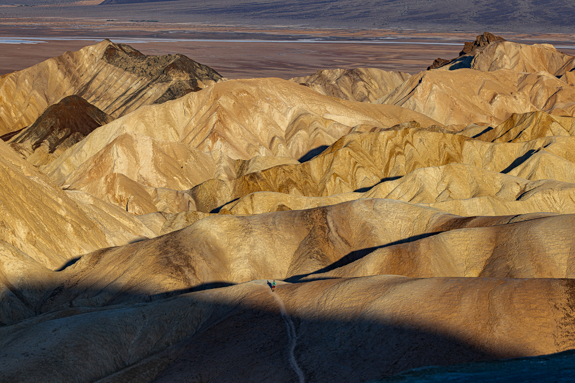 Wide composition of monumental Death Valley peaks with a small runner below, symbolizing endurance and resilience